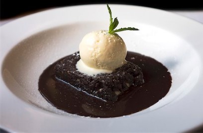 Hot Gooey Brownie topped with ice cream on a white plate